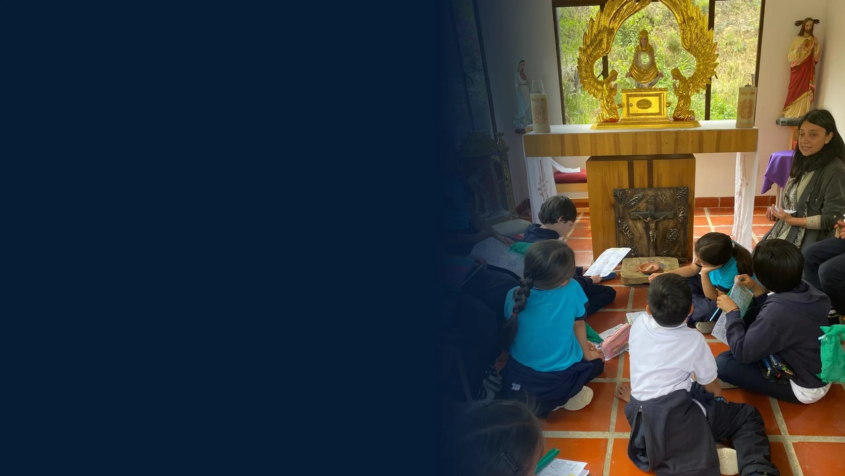 Estudiantes de primaria sentados en el piso de la capilla, frente al altar, con sus guías de trabajo y junto a una profesora