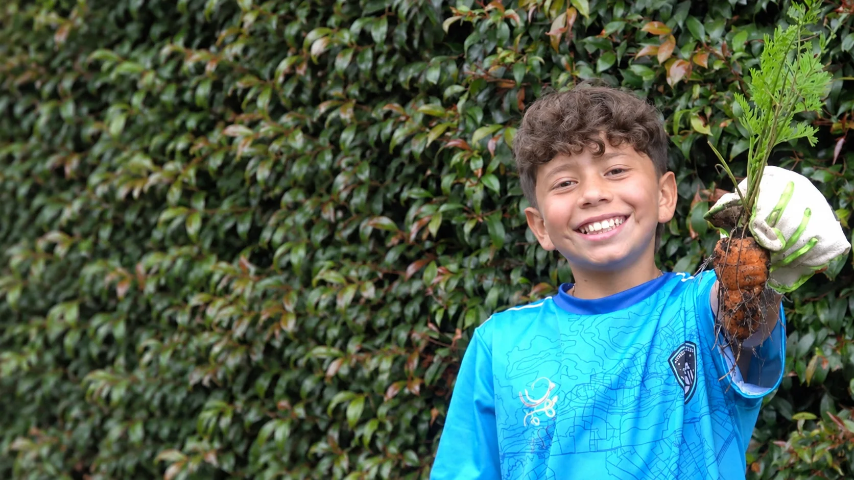 Estudiante del Gimnasio Santamaría de la Sabana sonriendo con una planta que acaba de sacar de la tierra