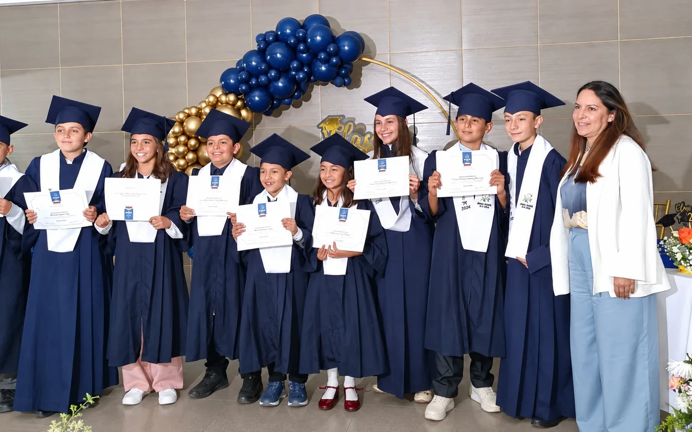 Estudiantes de primaria con toga y birrete, mostrando su diploma junto a una docente, en la ceremonia de grado