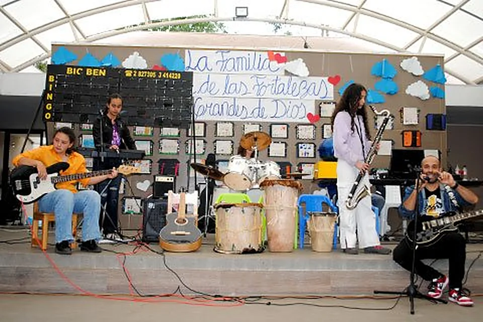 Estudiantes tocando guitarras, tambores y saxofón en una tarima bajo carpa