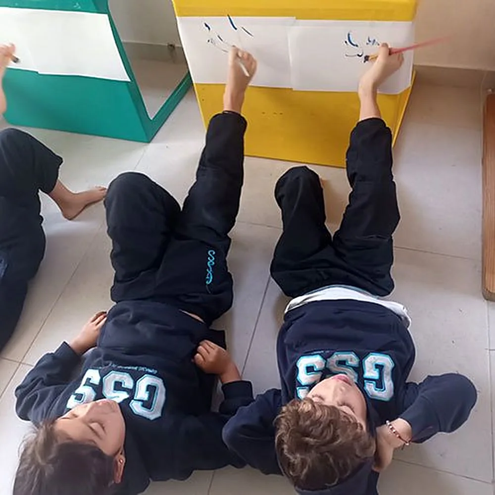 Niños de preescolar acostados en el piso dibujando sobre un papel pegado a la pared