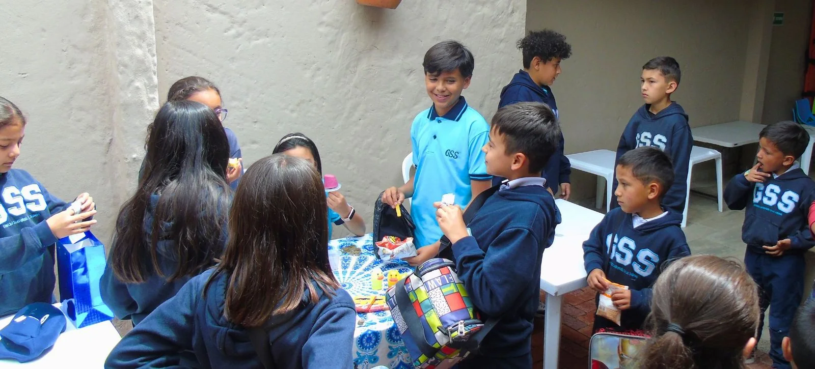 Estudiantes de primaria con el buzo del colegio reunidos alrededor de una mesa en el patio